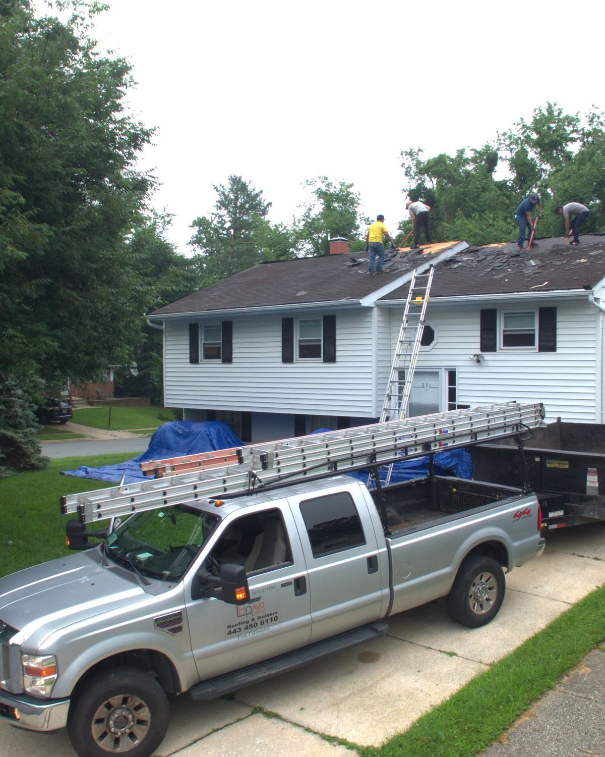 Bravo Roofing crew replacing the roof of a Maryland split-level home, with the company truck, dump trailer and ladders on the driveway