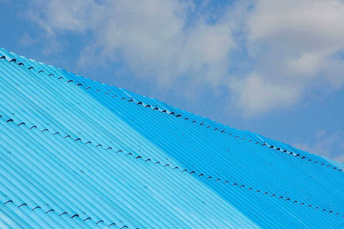 A bright blue corrugated roof viewed from below against a clear sky, representing roofing options for repairs.