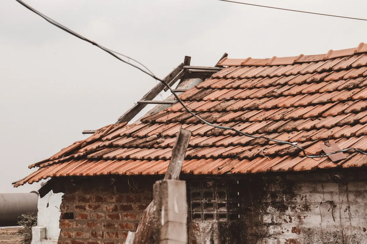 An old rural house with a damaged clay tile roof, highlighting the need for reliable roofing repairs.