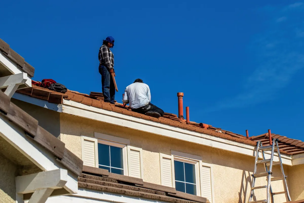 Workers installing tiles on a roof under a clear blue sky, highlighting the importance of skilled roofing services.