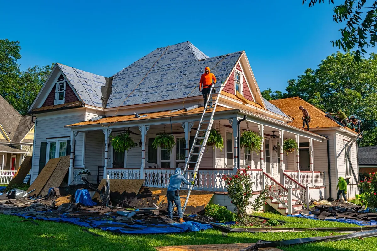 Roofers working on replacing the roof of a historic home, illustrating the importance of timely roof replacement.