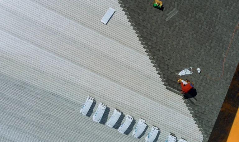 Aerial view of a building's roof being installed with new asphalt shingles, relevant to roof replacement timing.
