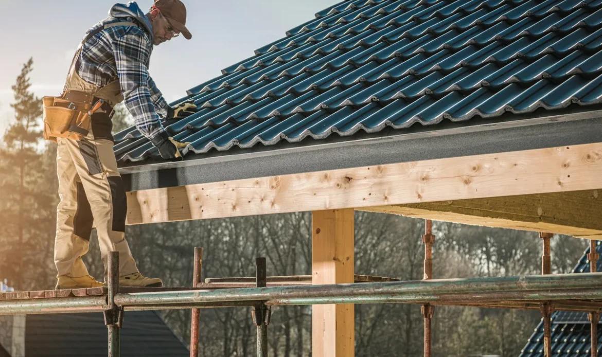 A builder installs a roof on a construction site under a clear blue sky, highlighting the importance of roof maintenance.