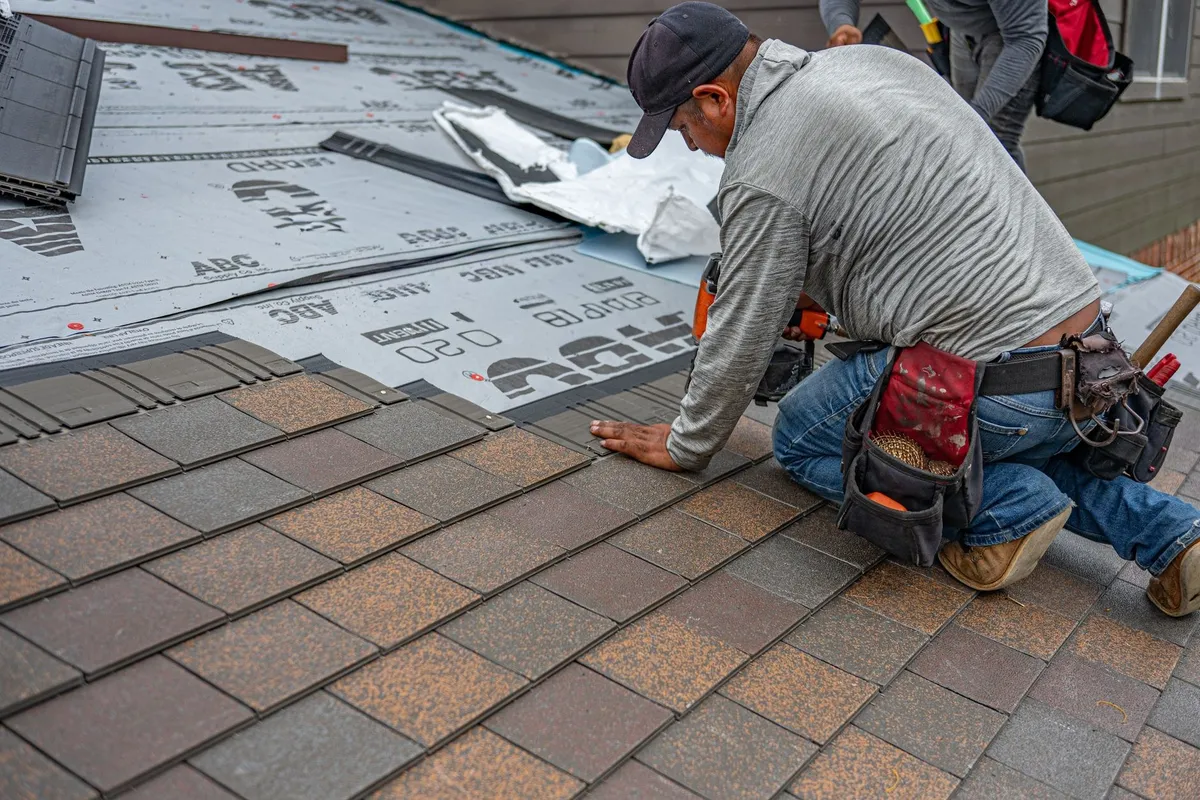 A skilled roofer installs asphalt shingles, highlighting the importance of roof maintenance and quality renovations.